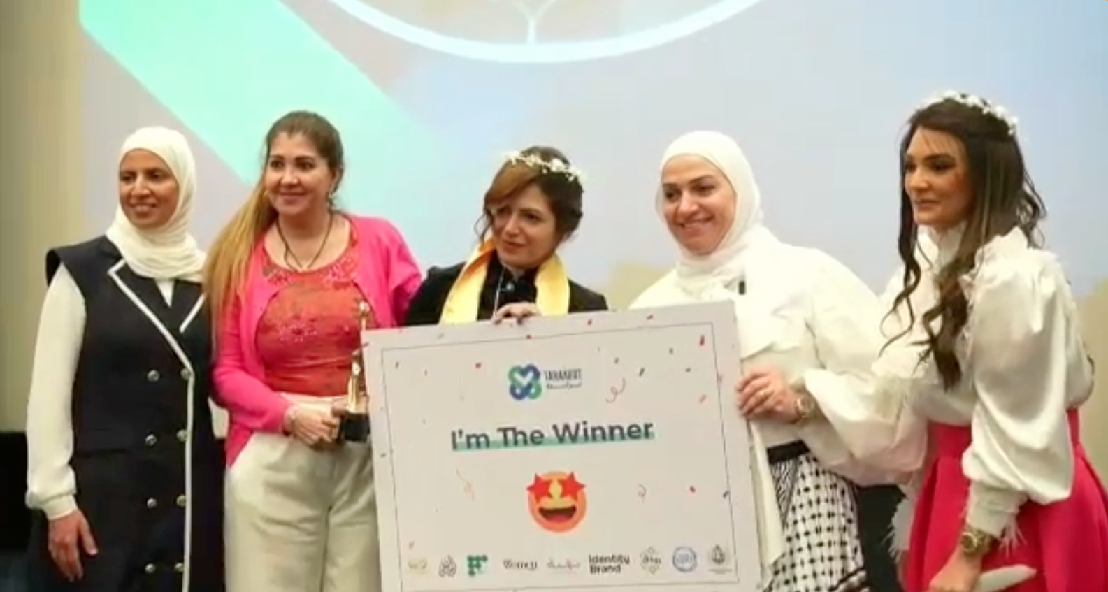 Dr. Mayada Elsabah on stage with fellow awardees holding an "I'm The Winner" sign