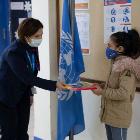 Dr. Mayada Elsabah handing UNICEF material to a schoolgirl during a community outreach visit