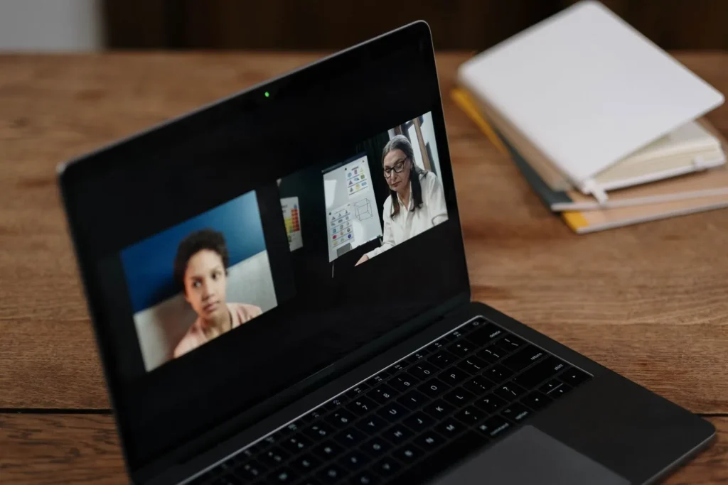 A laptop displaying a recorded professional webinar session beside a stack of notes