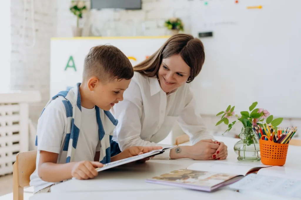 A specialist supporting a child during a one-to-one learning activity at a table in an ABAT training session
